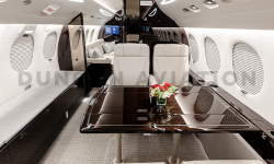 Beautifully refurbished interior of Falcon 7X showing cream leather chairs and dark wood table with cream and dark wood accents throughout
